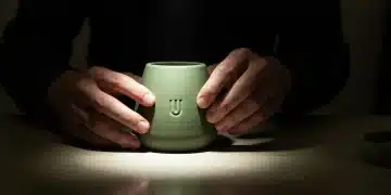 Close-up of hands gently touching a matte green ceramic product with an embossed logo, illuminated by dramatic chiaroscuro light, symbolizing deep brand resonance and customer connection.